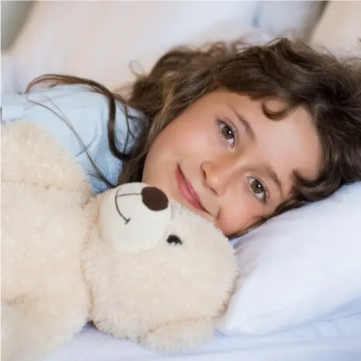 a child lies in bed with a teddy bear