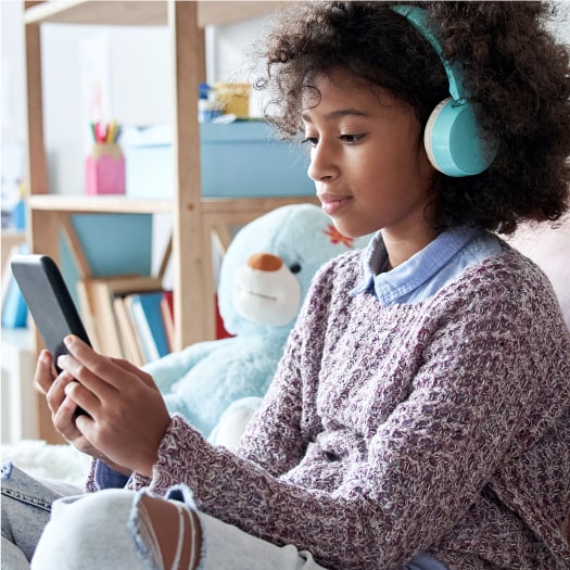 African american child kid girl wearing headphones holding phone sitting on bed
