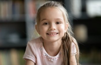 Head shot portrait smiling pretty little girl looking at camera, happy preschool child playing with camera, recording vlog, making video call, chatting online with relatives, using webcam