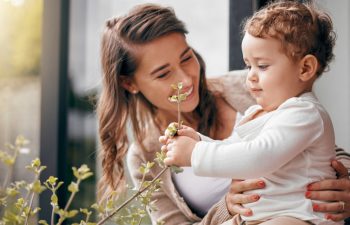 Happy woman, baby and together on porch for love, development and bonding at home. Mom, curious boy and touching plants outside for growth, trust and smiling with hug for joy, protection and wellness