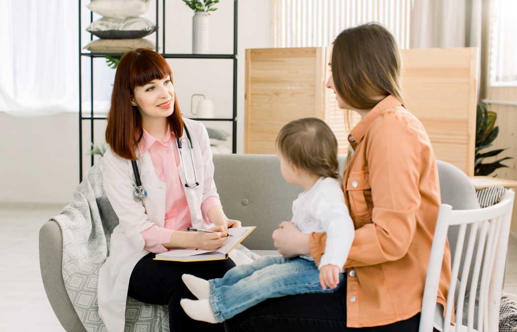 friendly young woman pediatrician doctor talks with mother of little baby girl after examination.